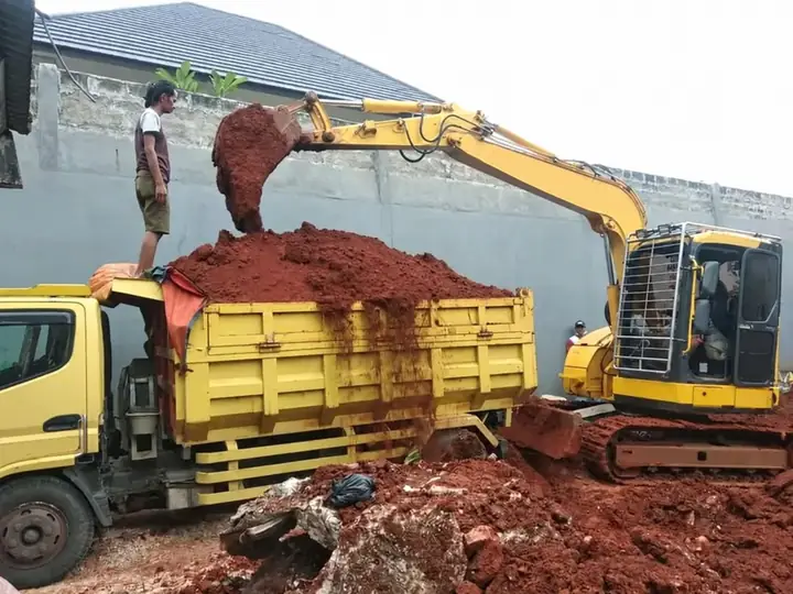 Ekskavator memuat tanah merah ke truk bak kuning