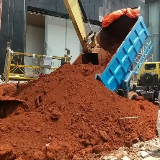 Truk bak biru menurunkan tanah merah di lokasi proyek