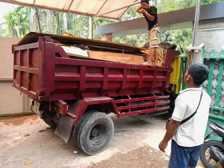 Truk bak merah marun dimuat petugas di depan bangunan