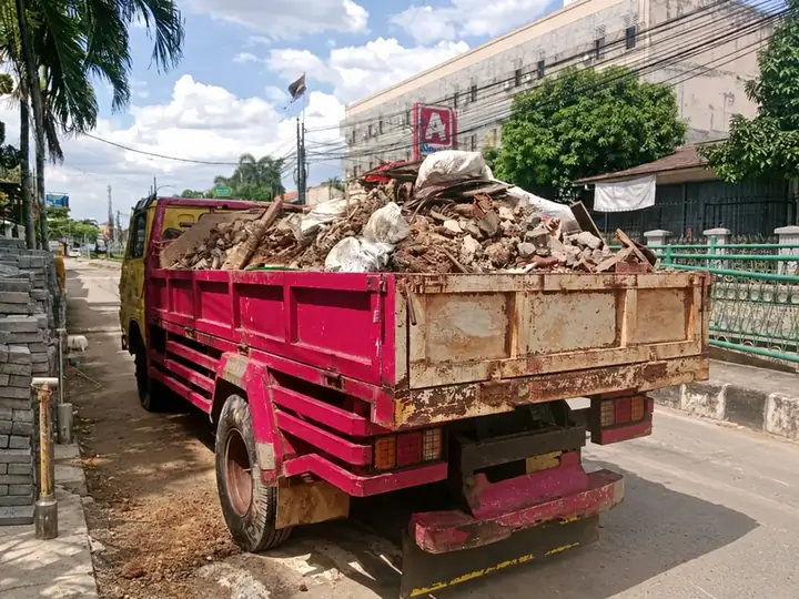 Truk bak merah muda bermuatan puing bongkaran di tepi jalan