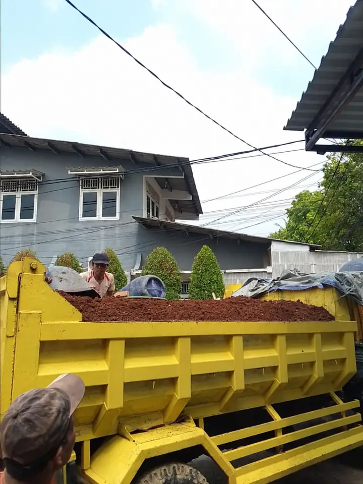 Bak truk kuning berisi tanah dan puing di tengah jalan
