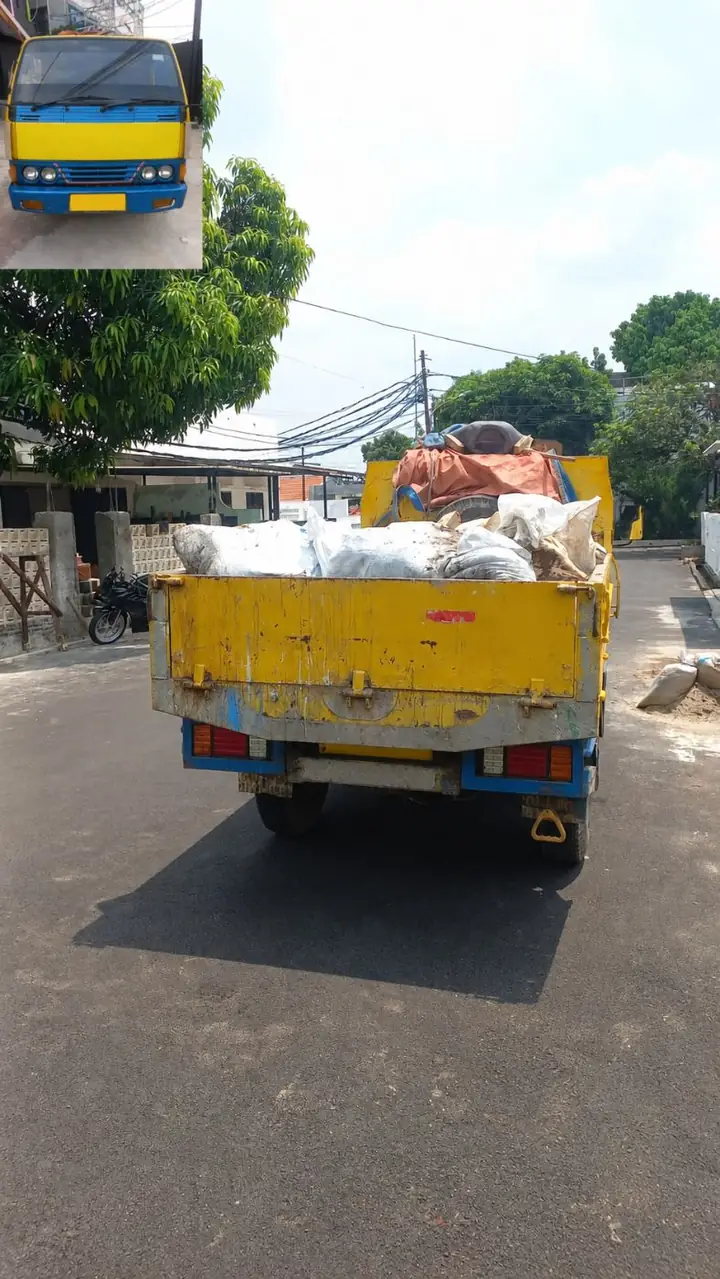 Truk bak kuning bermuatan karung dan puing di jalan permukiman